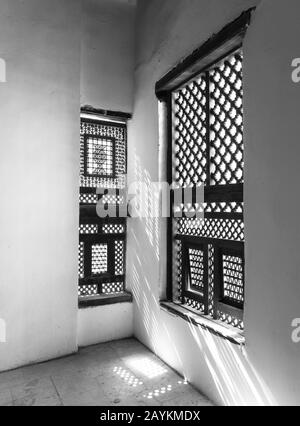 Schwarz-weiß von Ecke zweier verzierter Fenster aus Interleaved Grunge aus Holz - Mashrabiya - in Steinmauer am verlassenen Gebäude Stockfoto