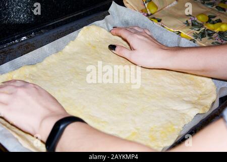 Ein junges Mädchen legt auf einem Backblech mit Pergamentpapier zum Backen eine dünne Schicht gewalzter Hefe-Pizza-Teig aus, gefettet mit Pflanzenöl. Basis für Stockfoto