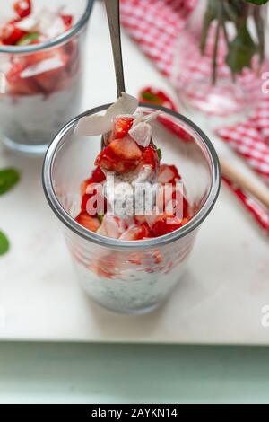 Blick über die Decke eines Glases mit Erdbeerstücken, gemischt mit chia-Samen, Honig, Minzblättern und Kokospänen und Milch. Stockfoto