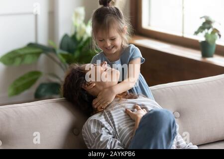 Fröhliche kleine Vorschultertochter, die den Hals der lachenden jungen Mutter umarmte. Stockfoto