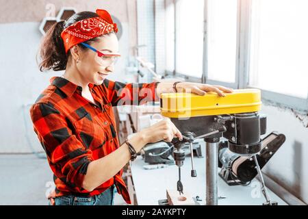 Eine starke und unabhängige Asiatin arbeitet an einer Bohrmaschine in einer Fabrik oder Werkstatt. Konzept mit blauem Kragen Stockfoto
