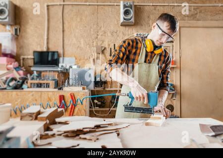 Zimmermann mit Nagelpistole Holzbretter in der Werkstatt krönt. Konzept der Handwerkerausrüstung Stockfoto