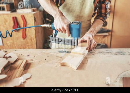 Zimmermann mit Nagelpistole Holzbretter in der Werkstatt krönt. Konzept der Handwerkerausrüstung Stockfoto