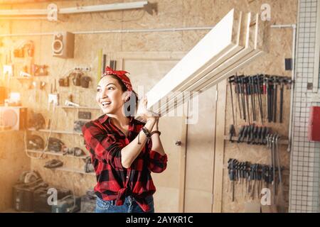 Asian Woman Worker mit Holzbrettern an der Schulter, dem Konzept der Arbeiter mit blauem Kragen und der Reparaturwerkstatt Stockfoto