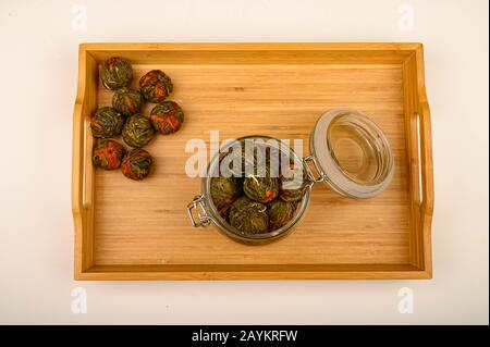 Eine Kugel Blumentee in einem Glasbecher auf einem Holztablett auf weißem Hintergrund. Nahaufnahme Stockfoto