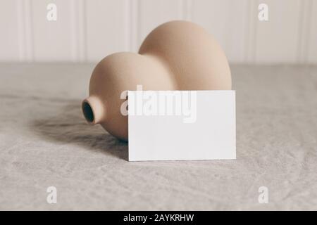 Nahaufnahme von leerer Visitenkarte und moderner organischer Keramikvase auf beigefarbenen Leinentischdecken. Leere Papierkarten-Mockup-Szene in neutralen Farben. Kunst, Stockfoto