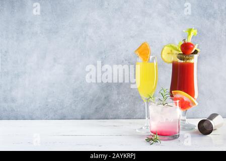 Brunch- oder Frühstückscocktails. Bloody Mary, Mimosa Drink und verschiedene erfrischende Cocktails aus Zitrusalkohol auf grauem Tisch, Kopierraum. Stockfoto