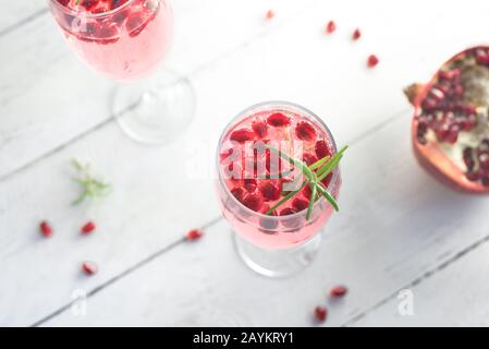 Mimosa-Cocktail mit Rosen-Champagner, Granatapfel und Rosmarin in Flötenbrille, Nahaufnahme. Mocktail, Mimosa Sekt Rosa Getränk. Stockfoto
