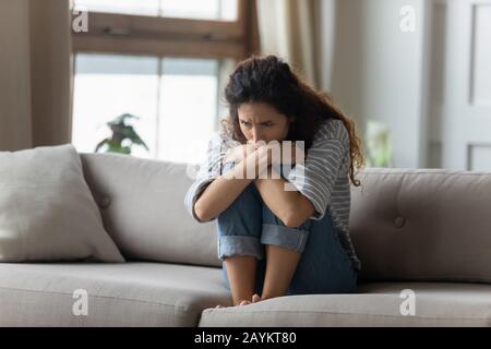 Betonte junge Frau, die Knie umarmte und allein auf der Couch saß. Stockfoto