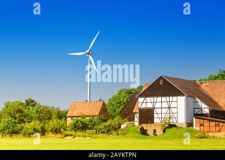 Windenergieanlagen, die sich auf dem Gelände des Betriebs in der Nähe des Erntefeldes im Vordergrund befinden. Landwirtschaft und Nachhaltiges Energiekonzept Stockfoto