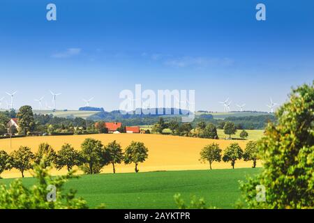 Windenergieanlagen, die sich auf dem Gelände des Betriebs in der Nähe des Erntefeldes im Vordergrund befinden. Landwirtschaft und Nachhaltiges Energiekonzept Stockfoto