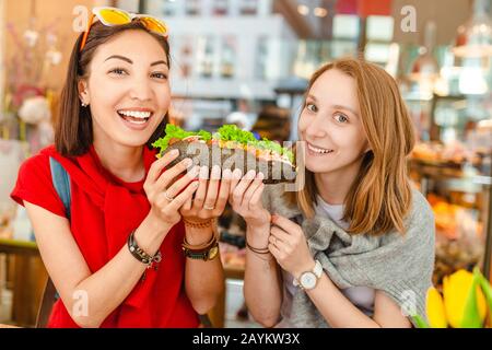 Fröhliche multirassische Freunde, die Sandwich essen und Spaß in einem Café haben Stockfoto