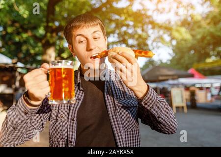 Junger Mann trinkt Bier im Freien Café und isst Heißhund Stockfoto