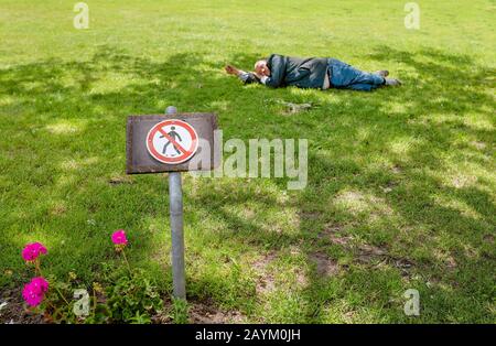 22. MAI 2018, LEIPZIG, DEUTSCHLAND: Obdachloser schläft auf dem Gras in der Nähe Des Verbotenden Schildes auf dem Rasen im Park Stockfoto