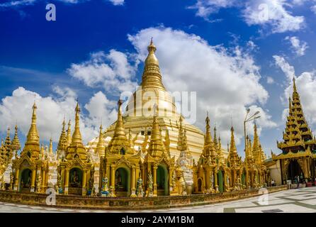 Pagoden umkreisen die Basis des vergoldeten Stupa der Shwedagon-Pagode, Yangon, Myanmar. Einige gebeten und Touristen ruhen unter der braunen Pagode. Stockfoto