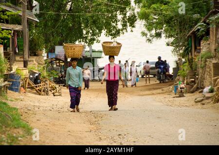 Myanmar-Frauen, die großen Bambuskorb auf dem Kopf tragen und auf der Sandstraße am Strand in Myanmar spazieren gehen Stockfoto