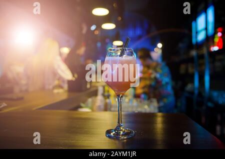 Pinkfarbener Cocktail mit zwei schwarzen Strohhalmen an der Theke. Geschenke und Geschenke für Kunden. Abstrakt verschwommene Restaurantbeleuchtung im Hintergrund Stockfoto