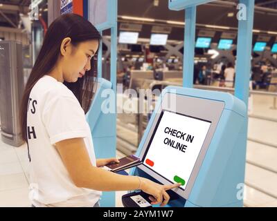 Junge Asianerin mit Reisepass, die einen interaktiven Touchscreen mit Selbstcheck-Kiosk am Flughafen verwendet und einen Selbstcheck für Flug oder den Kauf von Airplas macht Stockfoto