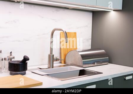 Wasserhahn und Waschbecken in modernem Küchendesign. Moderner Küchentisch mit Utensilien und Wasserspüle. Stockfoto