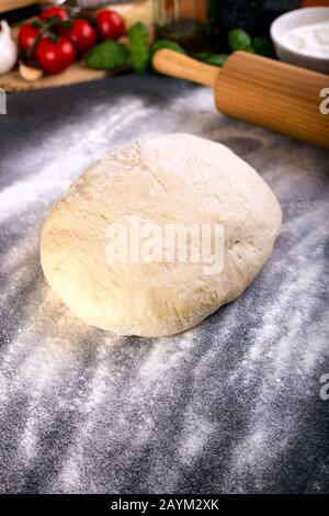 Pizzateig mit Holzrolle, Basilikum, Olivenöl und anderen Zutaten. Stockfoto