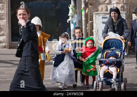 Jerusalem, ISRAEL - 15. MÄRZ 2006: Purim-Karneval. Ultraorthodoxe Frau mit Kindern, die die Straße überqueren.In Kostümen Gekleidete Kinder. Im berühmten Stockfoto