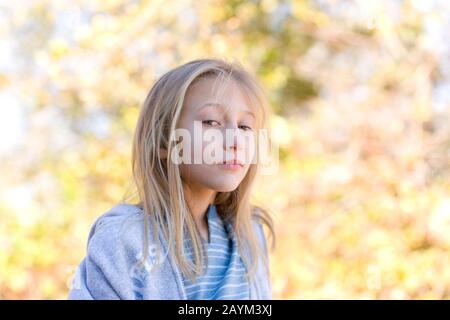 Ein selbstbewussteres, hübsches junges Mädchen mit blondem Haar und blauen Augen, das ein blaues Hemd und einen grauen Hoodie trägt. Stockfoto