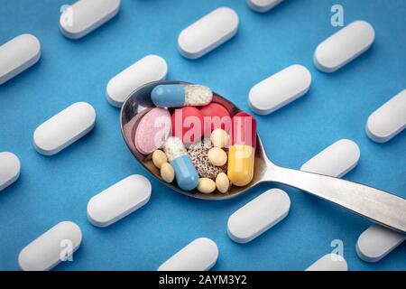 Bunte Pillen und Tabletten im Löffel mit Reihen weißer Tabletten im Hintergrund Stockfoto