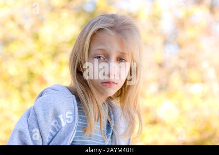 Ein introspektives, ziemlich junges, blondes, blauäugiges Mädchen mit trauriger Gesichtsausdruck, das einen grauen Hoodie trägt. Stockfoto