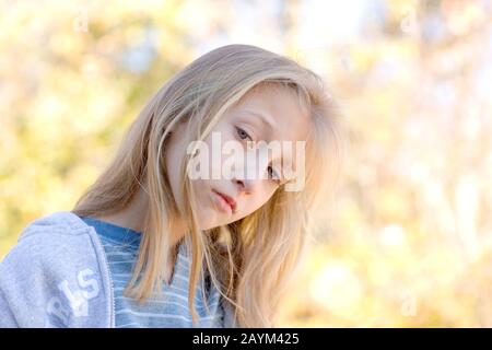 Ein selbstbewusstes, introspektives, hübsches junges Mädchen mit blondem Haar und blauen Augen, das ein blaues Hemd und einen grauen Hoodie trägt. Stockfoto