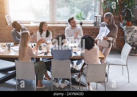 Junge Dame in hijab, die den Marketingbericht der Kollegen zeigt Stockfoto