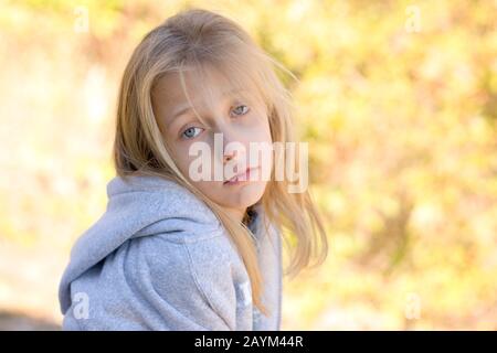 Ein introspektives, ziemlich junges, blondes, blauäugiges Mädchen mit trauriger Gesichtsausdruck, das einen grauen Hoodie trägt. Stockfoto