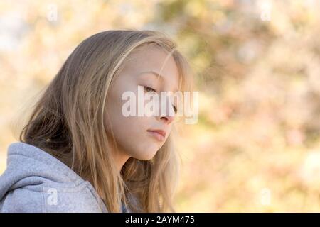 Ein introspektives, hübsches junges Mädchen mit blauen Augen und blonden Haaren mit grauem Hoodie. Stockfoto