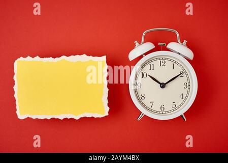 Weißer klassischer Wecker aus Vintage mit Glocken und leerem zerrissenem Papierblatt auf rotem Hintergrund. Design leer für Zeitkonzept Stockfoto