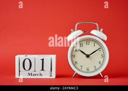 Weißer Retro-Wecker mit Glocken und Holzkalenderblöcken mit Datum 1. märz auf rotem Hintergrund Stockfoto