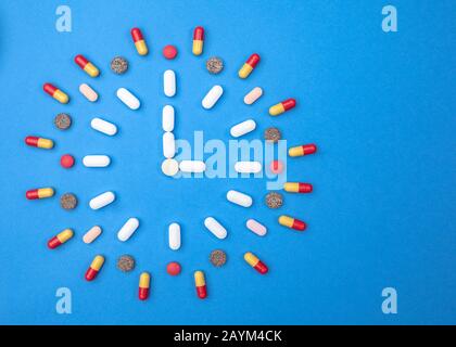 Verschiedene Arten von Pillen, die in Form einer Uhr auf blauem Hintergrund angeordnet sind. Pharmazie und Medizinkonzept Stockfoto