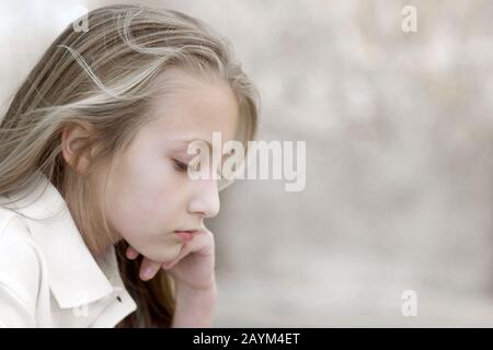 Ein introspektives, ziemlich junges Mädchen mit blondem Haar und blauen Augen, tief im Nachdenken. Stockfoto