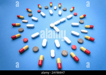 Verschiedene Arten von Pillen, die in Form einer Uhr auf blauem Hintergrund angeordnet sind. Pharmazie und Medizinkonzept Stockfoto