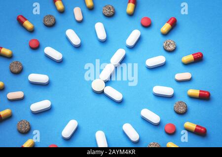 Verschiedene Arten von Pillen, die in Form einer Uhr auf blauem Hintergrund angeordnet sind. Pharmazie und Medizinkonzept Stockfoto