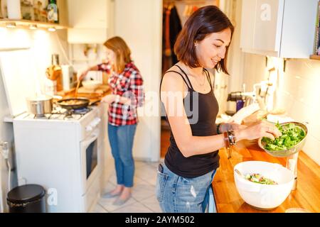 Zwei junge Frauen, die in ihrer Wohnung in der Küche zum Abendessen kochen Stockfoto