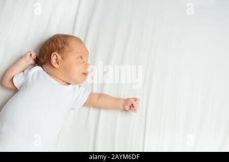 Portrait des neugeborenen Säuglings, der sich auf den Rücken im Raum legt und die Hand streckt Stockfoto