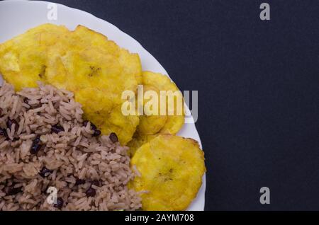 Nahaufnahme der weißen Platte mit Congris Reis traditionelle kubanische Küche mit gebratenen Pataconen. Auch bekannt als gallo Pinto mit Steinen. Stockfoto