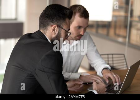 Kollegen aus verschiedenen ethnischen Gruppen, die mit einem Laptop arbeiten, der am Schreibtisch sitzt Stockfoto