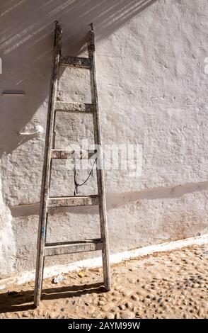 Weiß strukturierte verwitterte Wand mit einer stehenden alten Leiter aus Holz. Straße von Essaouira, Marokko. Stockfoto