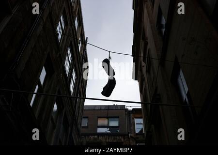 Ein Silhouettenbild von Schuhen, die durch die Schuhschnüre miteinander verbunden sind, hängt von einem elektrischen Draht in einer Gasse des Stadtgebietes von Glasgow, S Stockfoto