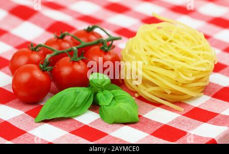 Unbehackte Tagliatelle, frische Kirschtomaten und frische Basilikumblätter auf rotem und weißem kariertem Tuch Stockfoto