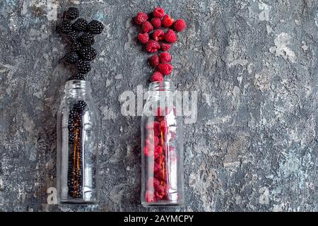 BlackBerry- und Himbeerobst in Glasflaschen mit Strohhalmen auf Steingrund. Frische Zutaten aus biologischem Smoothie. Superfoods und Health oder Detox Diätkost Lebensmittelkonzept. Stockfoto