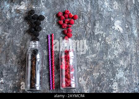 BlackBerry- und Himbeerobst in Glasflaschen mit Strohhalmen auf Steingrund. Frische Zutaten aus biologischem Smoothie. Superfoods und Health oder Detox Diätkost Lebensmittelkonzept. Stockfoto