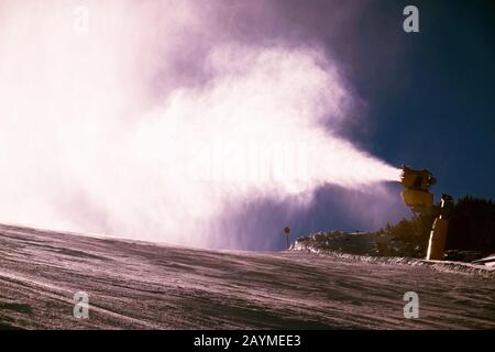 Schneekanonen arbeiten an der Skipiste in den Alpen am sonnigen Tag hart. Stockfoto