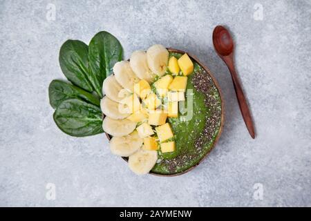 Smoothie-Spinat-Schüssel mit Banane und Mango, chia-Samen in Kokosschüsseln auf grauem Betongrund. Blick von oben. Stockfoto