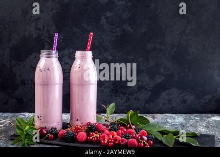 2 Gläser Milchshake oder Smoothie mit Preiselbeeren, Erdbeeren und Blaubeeren vor Steinkulisse. Stockfoto